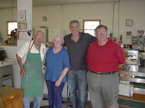 A group of four people, two men and two women, smiling together in a bright, casual indoor setting.