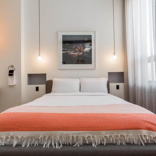 Cozy hotel room with a bed, orange throw blanket, and modern decor, featuring a framed picture and soft lighting.