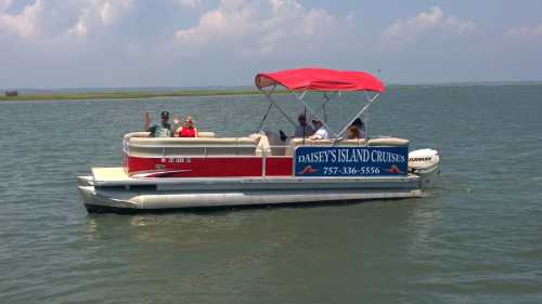 A red and white pontoon boat with passengers cruising on calm water under a blue sky.