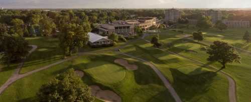 Aerial view of a golf course with lush green fairways, sand traps, and a clubhouse in the background.