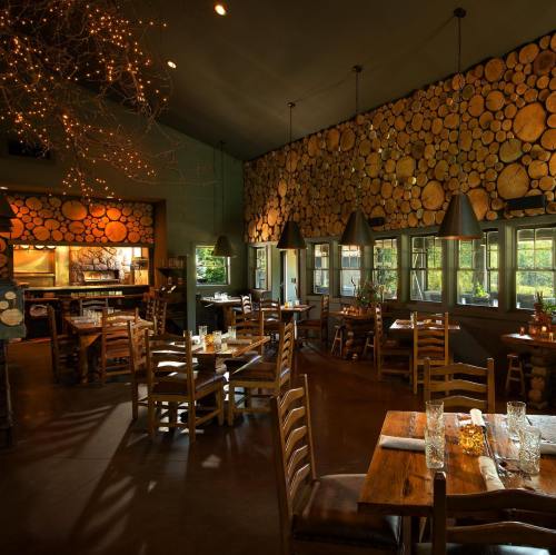 Cozy restaurant interior with wooden decor, tables set for dining, and warm lighting from hanging lamps.