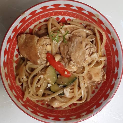 A bowl of chicken and vegetable pasta with herbs, featuring red chili and a colorful patterned rim.