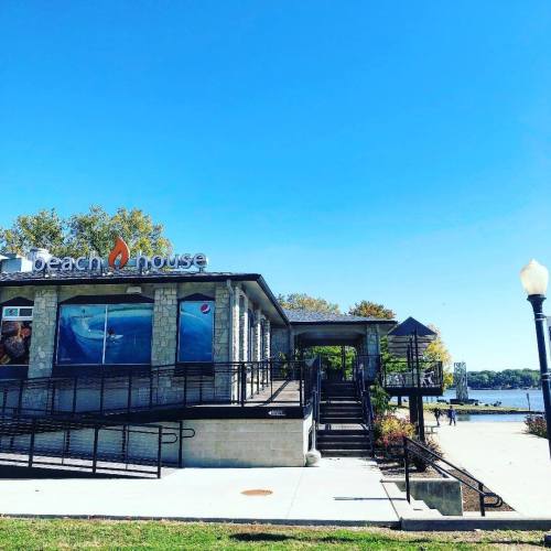A modern beach house restaurant by the water, featuring large windows and a clear blue sky.
