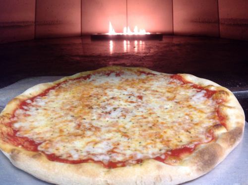 A freshly baked cheese pizza in front of a glowing wood-fired oven.