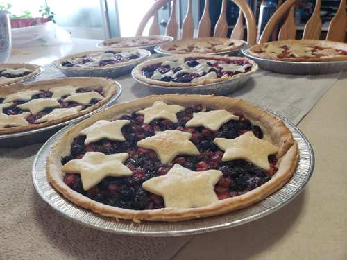 A table with multiple fruit pies, each topped with star-shaped crusts, arranged on a light-colored surface.