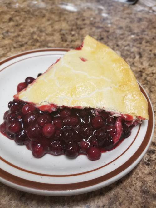 A slice of berry pie on a plate, with juicy berries spilling out from the crust.