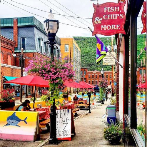 Colorful street scene with outdoor dining, flower planters, and a sign for a fish and chips restaurant.
