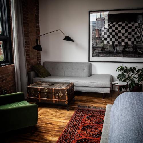 A cozy living room with a gray sofa, a vintage coffee table, a green chair, and a large wall art piece.