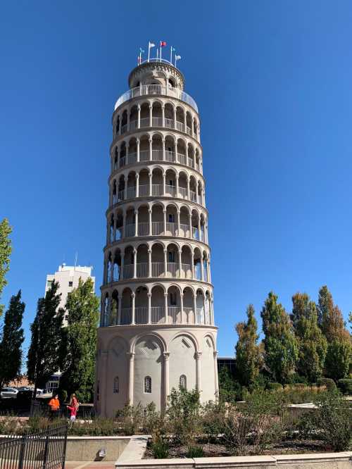 A replica of the Leaning Tower of Pisa surrounded by trees and a clear blue sky.