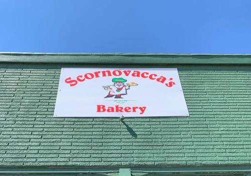 Sign for Scornovacca's Bakery featuring a cartoon chef holding baked goods against a blue sky.