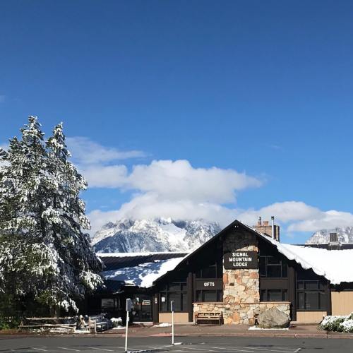 A lodge surrounded by snow-covered mountains under a partly cloudy sky. Trees are dusted with snow.