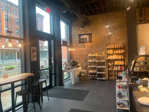 Cozy café interior with brick walls, shelves of snacks, and large windows letting in natural light.