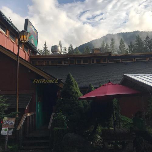 A rustic building with a sign reading "Entrance," surrounded by trees and mountains in the background.