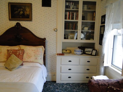 Cozy bedroom with a floral bedspread, wooden headboard, and a bookshelf filled with books and decorative items.