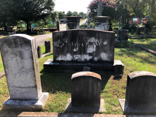 Gravestones in a cemetery, with a prominent headstone reading "Hemingway" surrounded by smaller stones.