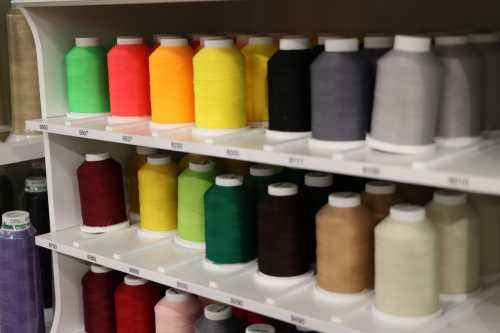 Colorful spools of thread arranged on shelves, featuring various shades of green, yellow, black, and more.