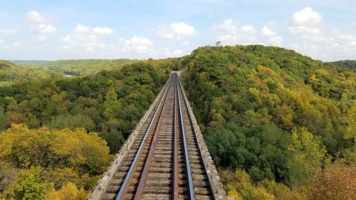 A view of railway tracks stretching into the distance, surrounded by vibrant autumn foliage and a blue sky.