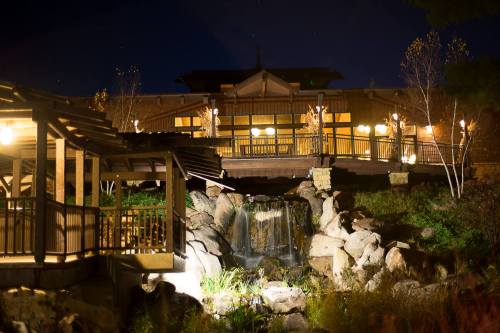 A serene night scene of a building with lights, overlooking a small waterfall and rocky landscape.