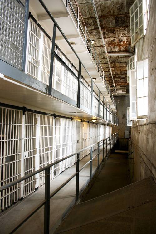 A long corridor in a prison with barred cell doors on either side and a high ceiling.