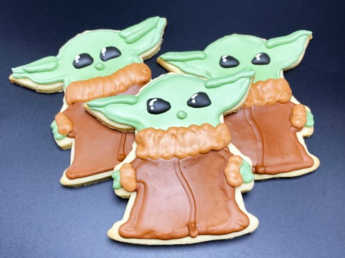 Three decorated cookies shaped like a green character with large ears, wearing a brown robe and a textured collar.
