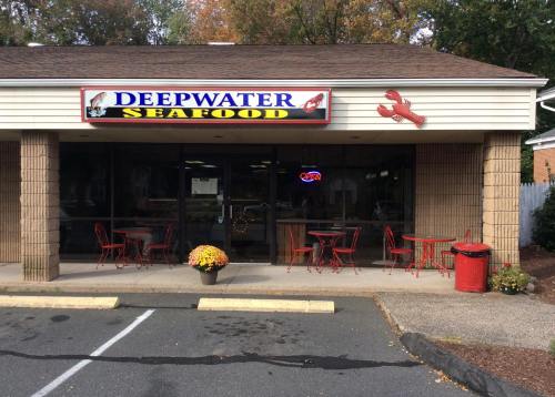 Exterior of Deepwater Seafood restaurant with a sign, outdoor seating, and a "Open" neon sign.