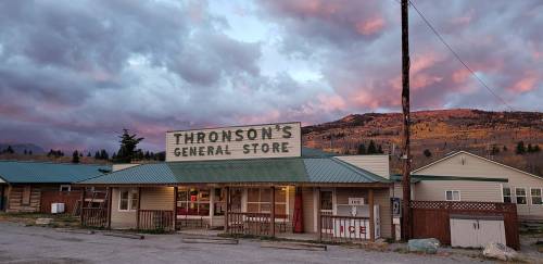 A rustic general store with a sign reading "Thronson's General Store," set against a colorful sunset and mountains.