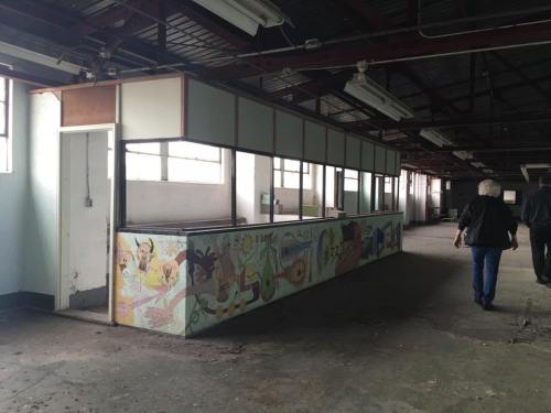 An empty, abandoned room with a colorful mural on a counter and two people walking away.