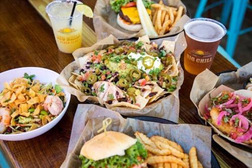 A spread of delicious food including nachos, a burger, fries, a salad, and a drink on a wooden table.