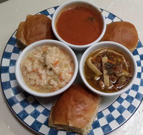 A plate with three bowls of soup and a side of bread rolls, featuring a variety of colorful ingredients.