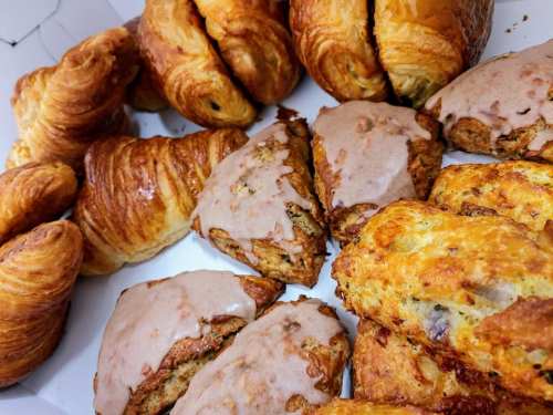 A variety of baked goods including croissants, scones with icing, and pastries arranged in a box.