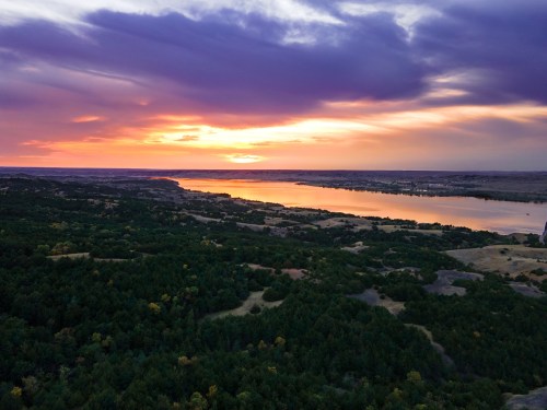 A vibrant sunset over a calm lake, surrounded by lush greenery and rolling hills.