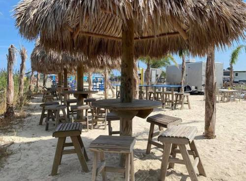 A sandy outdoor area with thatched-roof tables and benches under a clear blue sky.