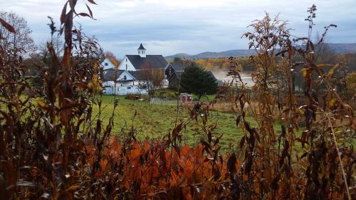 A scenic view of a rural landscape with a church, houses, and autumn foliage in the foreground.