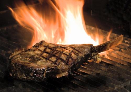 A juicy steak sizzling on a grill with flames rising around it, showcasing grill marks and a rich, smoky color.