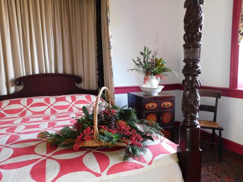 A cozy bedroom featuring a quilted bedspread, a decorative basket of greenery, and a floral arrangement on a dresser.