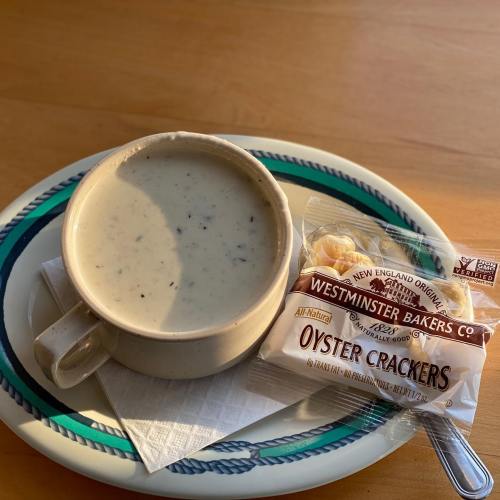 A bowl of creamy clam chowder next to a pack of oyster crackers on a plate with a napkin.