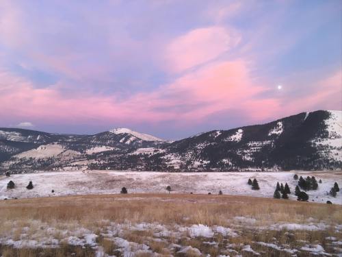A serene landscape at dusk, featuring rolling hills, snow-covered fields, and a pastel pink sky with a hint of moonlight.