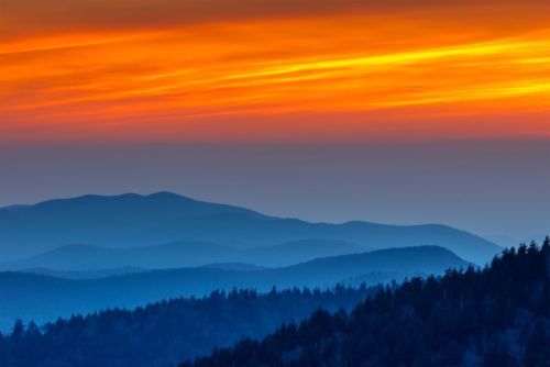 A stunning sunset over layered blue mountains, with vibrant orange and yellow hues in the sky.
