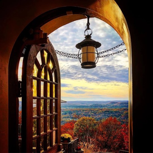 A wooden door opens to a scenic view of colorful autumn trees and a cloudy sky. A lantern hangs above the doorway.