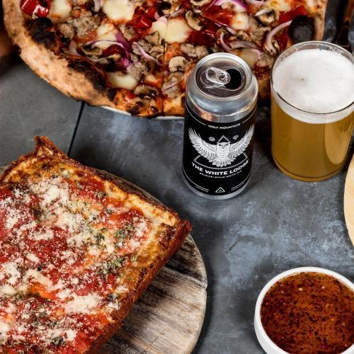 A spread of pizza, craft beer, and a side of marinara sauce on a rustic table.
