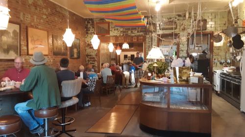 A cozy restaurant interior with patrons dining, exposed brick walls, and colorful decorations overhead.