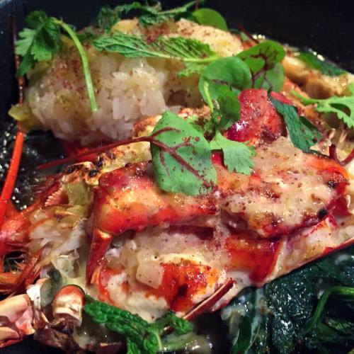 A close-up of a dish featuring crab on rice, garnished with herbs and spices, served in a black bowl.