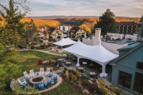 A scenic view of a resort with white tents, a fire pit, and autumn foliage in the background.