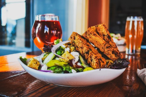 A vibrant salad with croutons and feta cheese, accompanied by two slices of bread and a glass of red beverage.