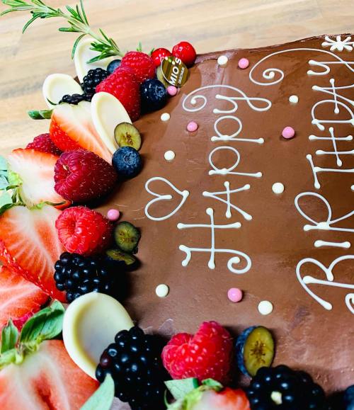 A chocolate birthday cake decorated with fresh berries, chocolate curls, and colorful sprinkles.