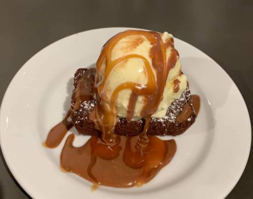 A slice of chocolate cake topped with vanilla ice cream and drizzled with caramel sauce on a white plate.