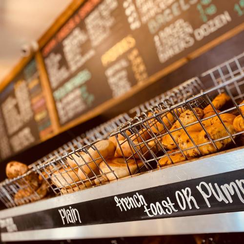 A wire basket filled with various baked goods, with a chalkboard menu in the background displaying items and prices.