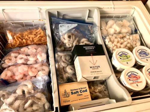 A freezer filled with various seafood items, including shrimp, mussels, and salt cod, along with containers of crab dip.