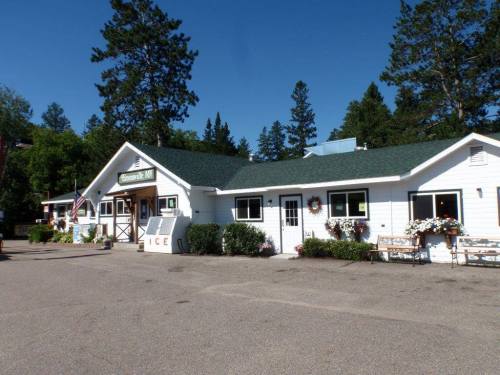 A white building with a green roof, surrounded by trees, featuring a sign and flower planters outside.