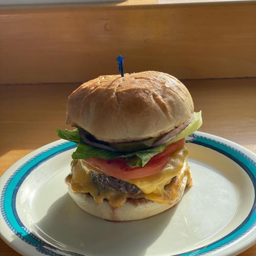 A cheeseburger with lettuce, tomato, and a blue candle on a plate, sitting on a wooden surface.